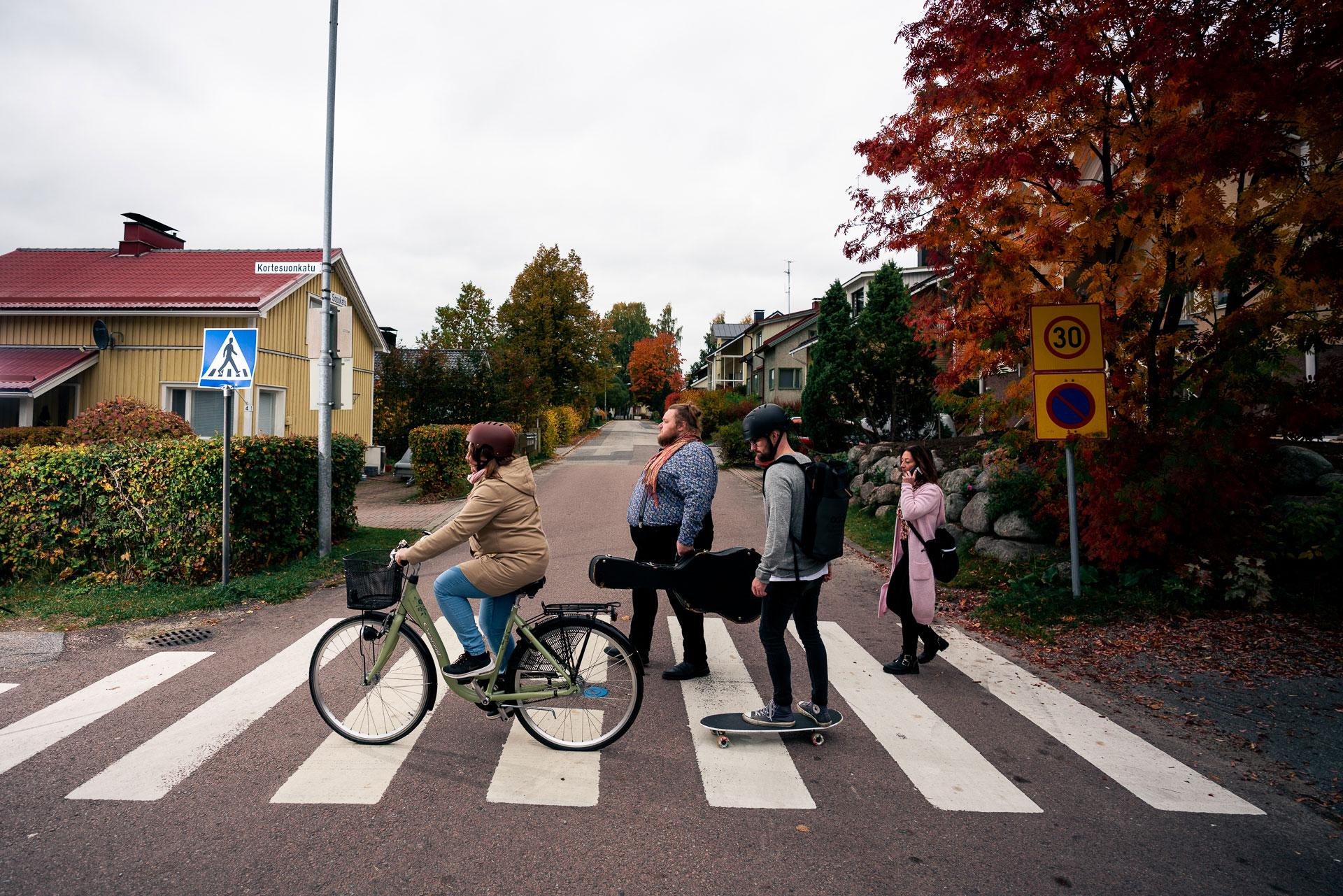 Neljä henkilöä ylittää suojatietä kävellen, pyörällä ja rullalaudalla.