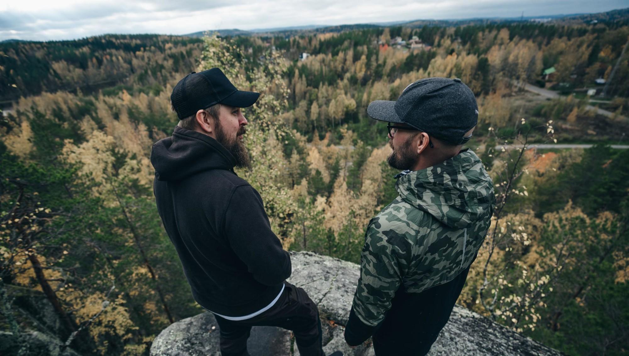 Two men are standing on a big rock.