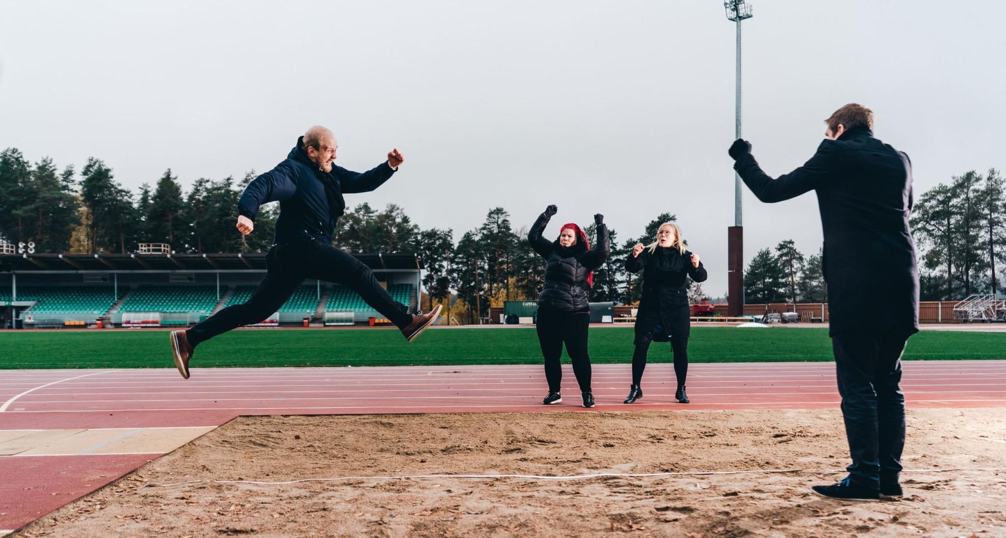 A man doing a long jump while others cheer for him.