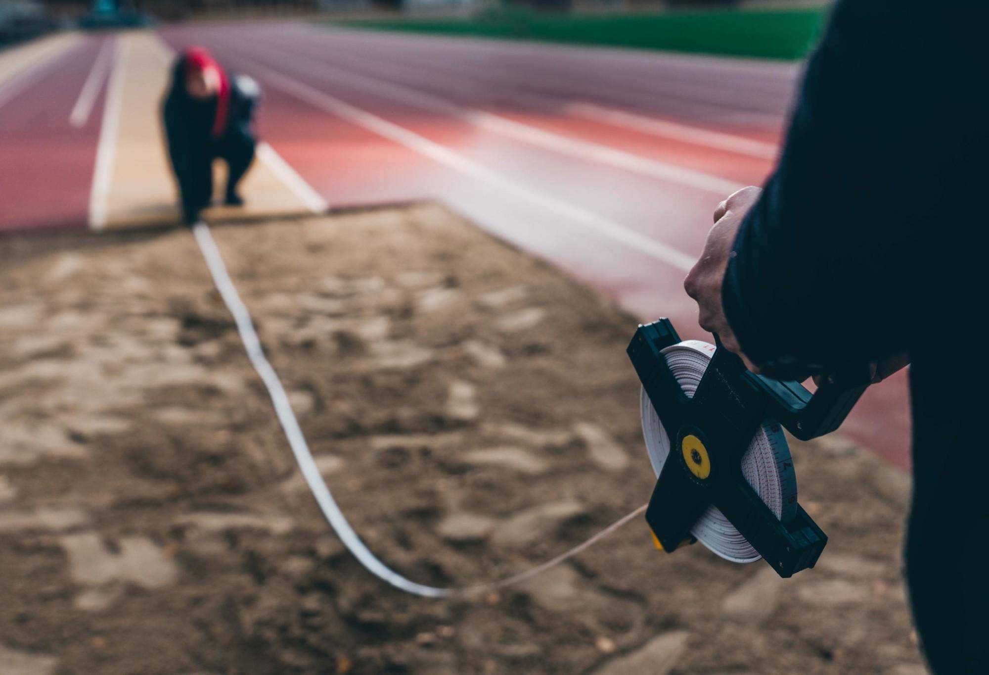 Two persons measure a long jump result.