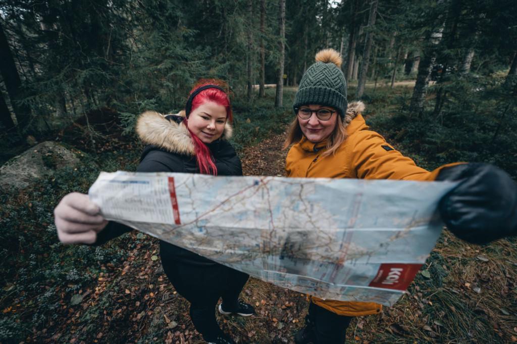Kaksi naista katselee paperikarttaa metsässä.